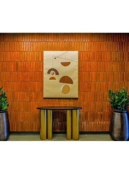 A simple console table stands against a warm, terracotta-colored brick wall, accented by a modern art piece. This vignette adds a touch of artistic flair to the clubhouse common area.