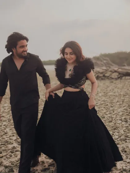 A candid walking shot on the beach, capturing the natural interaction and movement of the couple in their elegant black attire.