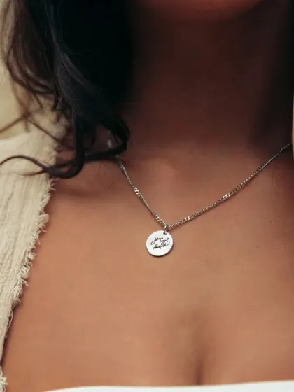 A woman wearing a silver-toned round pendant with a custom design. This image shows the delicate size and placement of the pendant for everyday wear.