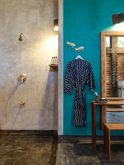A bathroom at Jalakara that combines polished cement walls with a vibrant teal accent wall and custom wooden furniture.