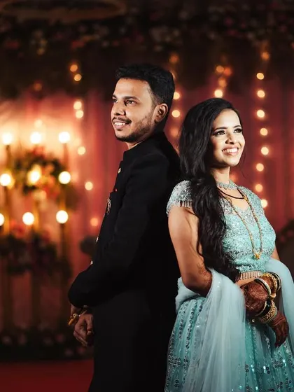 Shweta and Onkar standing back-to-back against a backdrop of twinkling lights. This classic pose is elevated by the beautiful bokeh, creating a festive and romantic atmosphere.