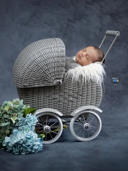 A similar setup with the grey wicker pram, this time against a deep blue, textured background with a floral accent, showing how we can customize a classic look.
