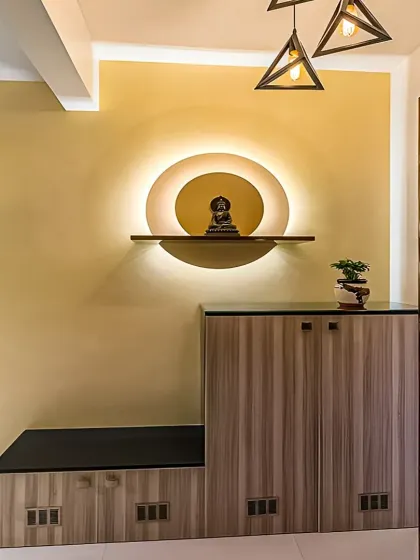 This foyer unit creates a serene entrance with a backlit circular niche for a small statue. The design includes a shoe cabinet with a seating bench, combining spiritual and practical elements.