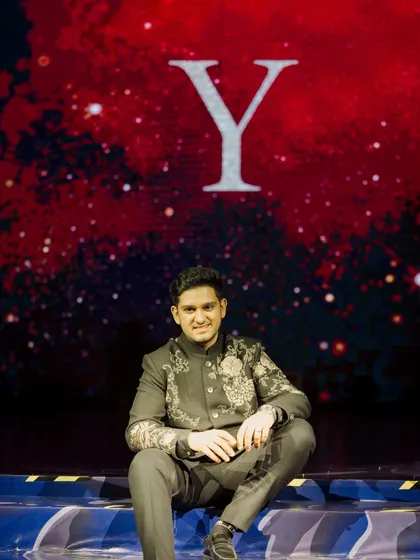 A quiet moment before the show. The groom sits on the edge of the stage, with his initial projected on the giant LED screen behind him, ready for his big performance.