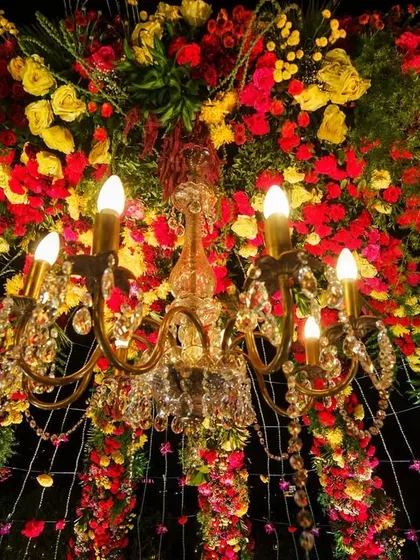A close-up shot looking up into a crystal chandelier surrounded by a dense arrangement of red and yellow flowers, showcasing intricate ceiling decor.
