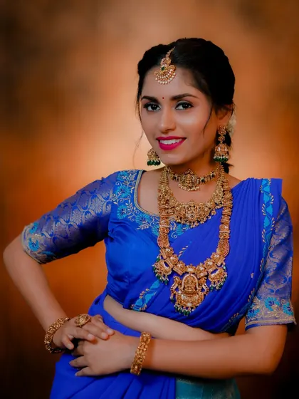 A model showcasing a traditional antique gold set with a long haaram and choker against a vibrant blue saree. This demonstrates how to style classic jewellery for a bold look.