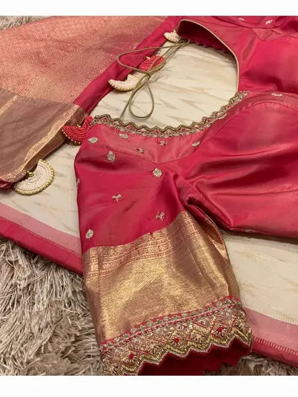 A close-up of the sleeve and tassels of the red blouse and off-white saree combination.