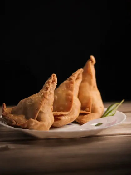A close up of three crispy samosas on a plate, with the focus on their texture and golden brown color.