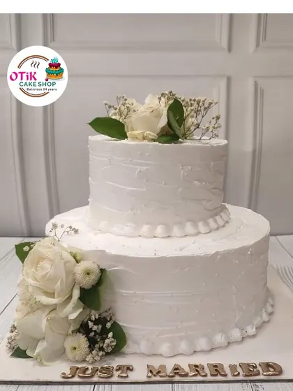 A classic two-tiered "Just Married" cake, perfect for an intimate wedding celebration. The textured white buttercream is adorned with fresh white roses for a look of pure and simple elegance.