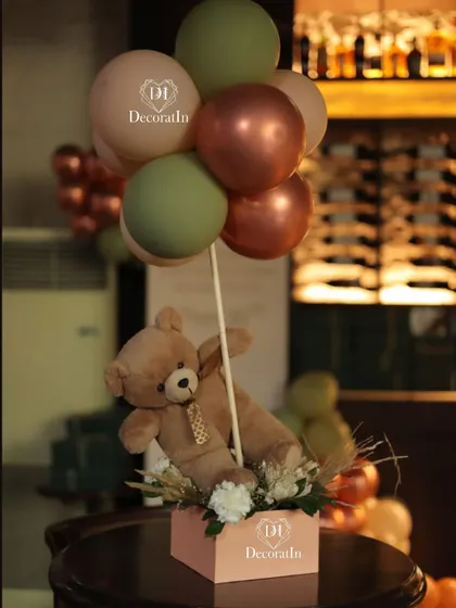 A close-up of a teddy bear centerpiece, showing the mix of matte and metallic balloons.