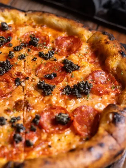 A close-up on a classic Pepperoni Pizza, this time with a sprinkle of black olive tapenade for an extra layer of salty, briny flavor. It's a simple twist that elevates a classic.