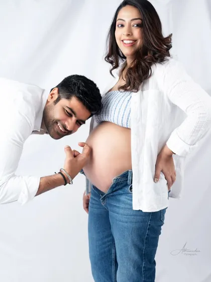 A playful and cute moment. The dad-to-be points at the baby bump, a fun way to interact and create a happy memory.