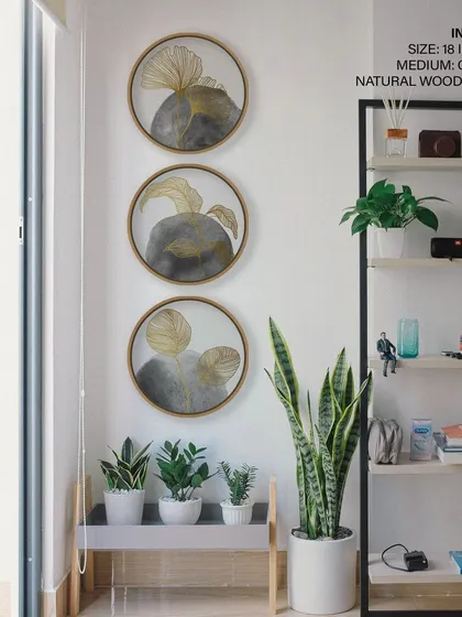 This set of three circular prints features minimalist botanical designs with golden leaves on a grey watercolor background. The natural wood frames add warmth to the cool, sophisticated color palette.