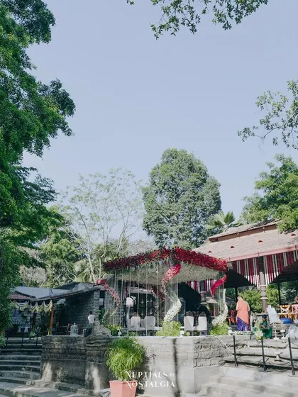 A wide-angle view showcasing the stunning floral mandap in the context of the beautiful heritage venue, The Tamarind Tree. The design complements the natural surroundings while creating a grand statement.