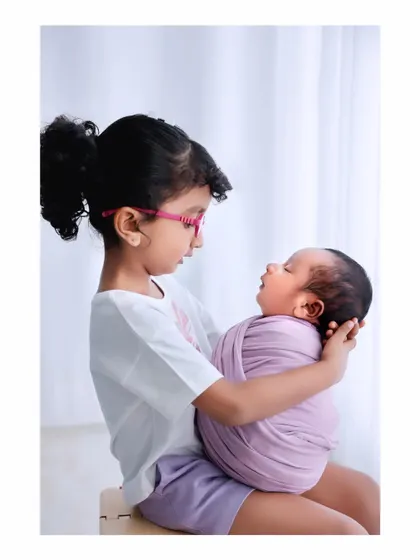 A sweet moment between siblings as an older sister in glasses carefully holds her newborn sibling. This photo is a perfect example of a newborn and sibling photoshoot.