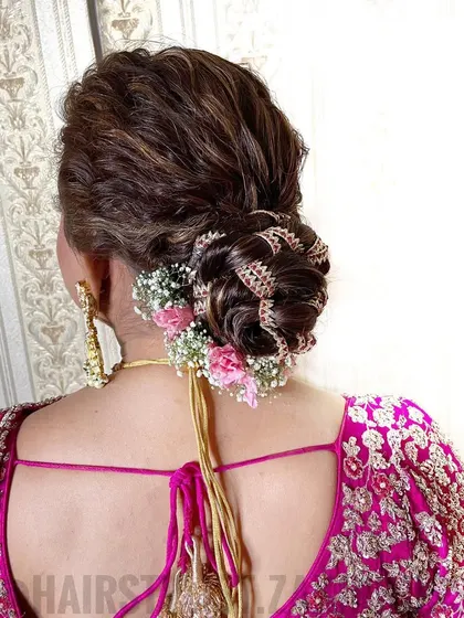 This bridal bun features intricate weaving and is decorated with a golden gota patti accessory. I added fresh pink carnations and baby's breath to match the bride's pink lehenga.