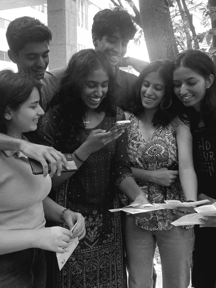 A group of friends huddle together, laughing as they look over their newly printed photo strips. It's a shared moment of joy.
