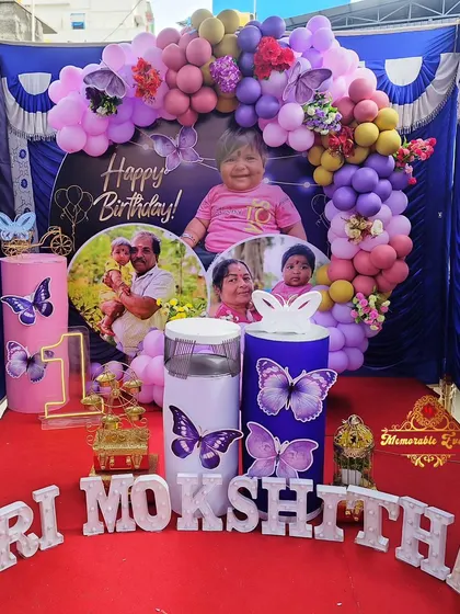 A personalized butterfly-themed birthday setup featuring photos of the birthday girl on the backdrop and plinths.