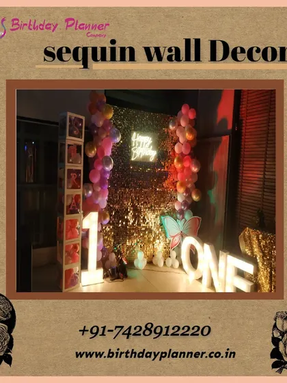 A glamorous first birthday celebration using a gold sequin wall. The setup is personalized with a photo display strip, large 'ONE' marquee letters, and a colorful balloon garland.