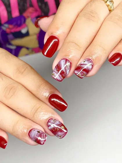 A beautiful red and white marble design with gold foil accents on short, square nails.