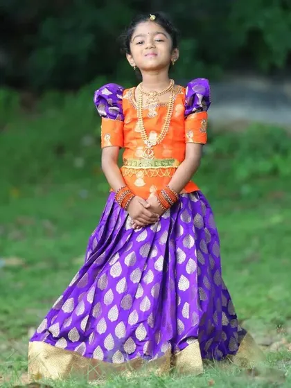 A full view of the custom Pattu Pavadai I made for the elder sister. The vibrant orange blouse with traditional puffed sleeves pairs beautifully with the royal purple silk skirt featuring a gold leaf pattern.