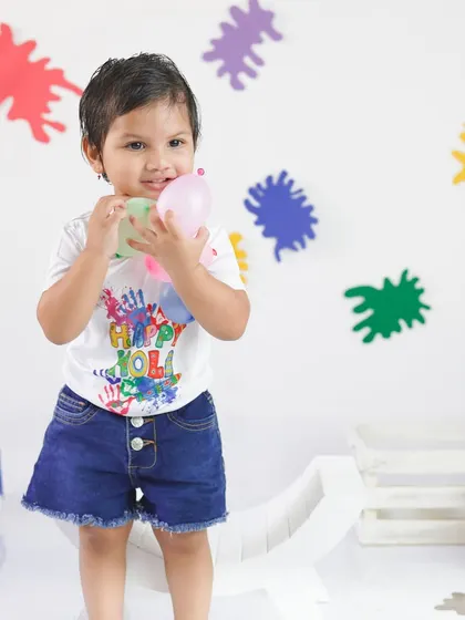 Holding colorful water balloons, this little girl is ready for Holi fun. Her 'Happy Holi' t-shirt adds to the celebratory feel of the shoot.