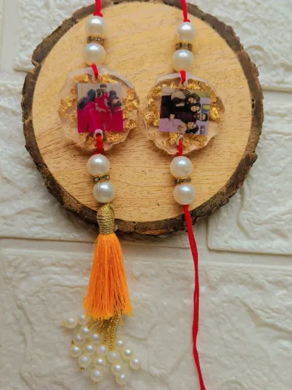 A beautiful pair of photo rakhis made with resin, gold flakes, and pearls. One features a tassel, making it a perfect lumba for your bhabhi.