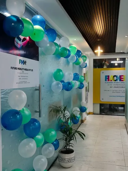 A balloon garland in shades of blue, green, and white, arranged along the glass wall of an office for a celebration.