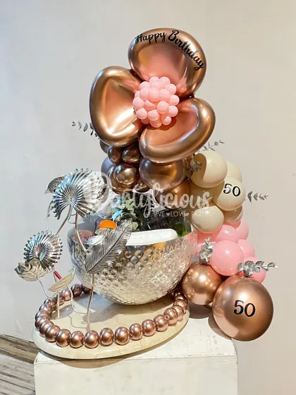 A luxurious 50th birthday gift arrangement in rose gold and pink, combining balloons with a beautiful silver bowl and decorative accents.