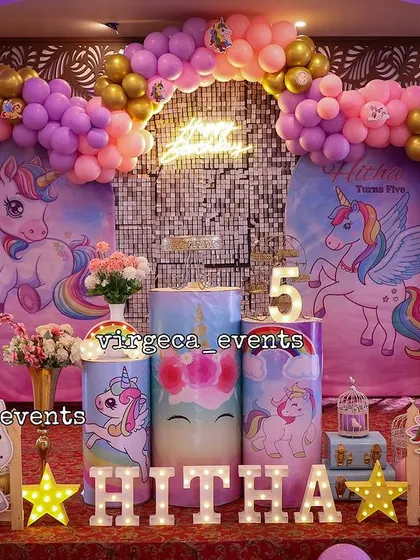 A vibrant and fun unicorn-themed birthday party. The setup is filled with color, from the rainbow balloon arch to the multiple unicorn character cutouts.