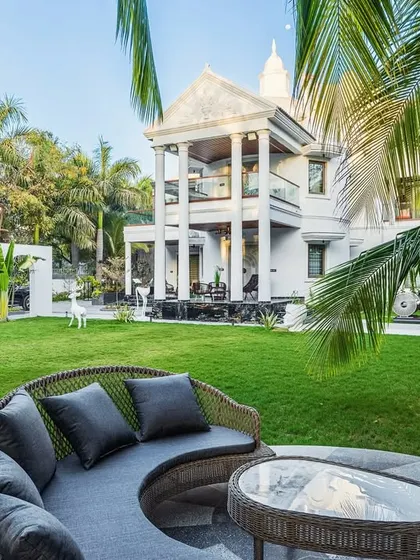 A daytime view of the Tropical Manor's garden and circular deck. The design fuses modern gothic architecture with a tropical landscape, creating a sense of grandeur and tranquility. The towering palms frame the villa, lending it a regal and timeless charm.