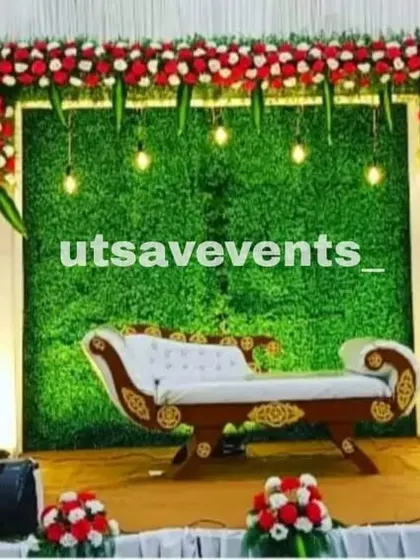 A simple and elegant reception stage with a green grass wall backdrop framed by red and white flowers. The hanging Edison bulbs add a touch of modern charm.