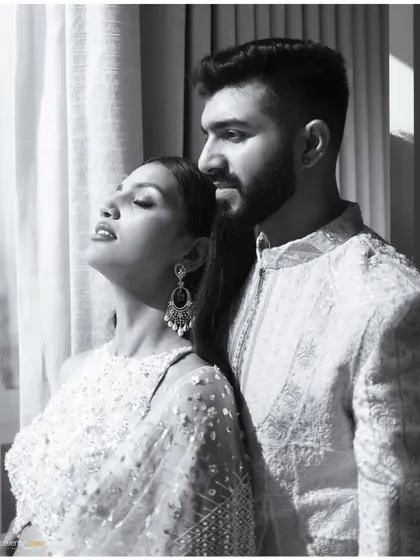 A serene black and white portrait of a couple, bathed in soft window light. Her eyes are closed in contentment as she leans into him.