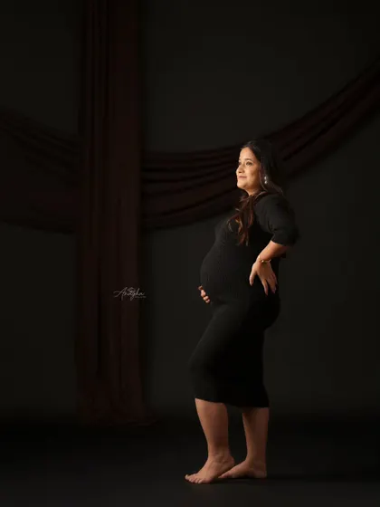 A full-length profile shot in a classic black dress against a dark backdrop. This pose is perfect for elegantly showcasing the silhouette of the baby bump.