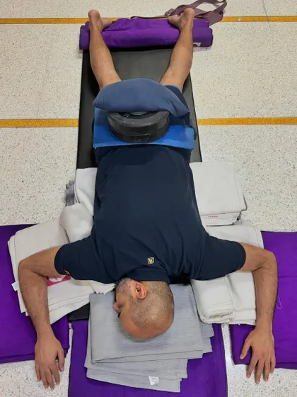 This is an elaborate setup for a deep restorative pose. The extensive use of props, including bolsters and weights, ensures the body is completely supported, facilitating a profound state of relaxation and healing.