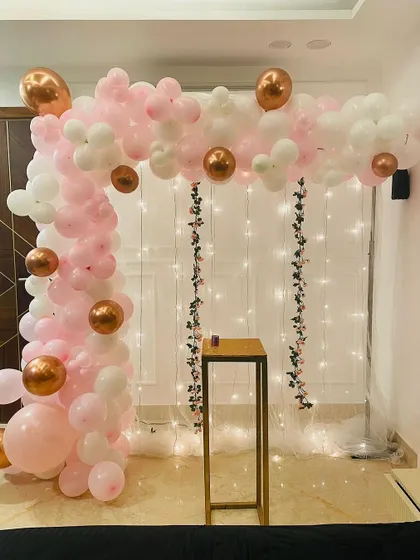 For a simple yet beautiful decoration, we created this balloon arch in soft pink, white, and rose gold. The backdrop is a sheer curtain with fairy lights, adding a touch of warmth and magic to the celebration space.