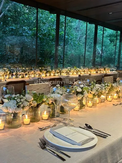 The Central Pavilion at night, with a long dining table aglow with dozens of candles. The floor-to-ceiling windows reflect the intimate scene, while revealing the dark forest outside.