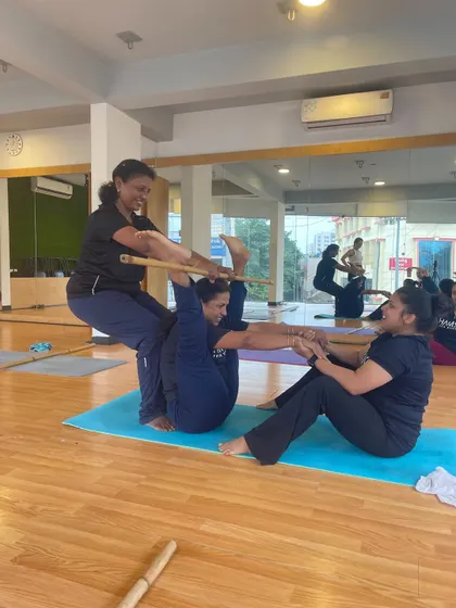 Teamwork makes the dream work! Three students collaborate on a complex partner pose using a stick for support and connection.