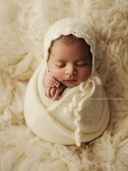 Simplicity at its most beautiful. A newborn wrapped snugly in creamy white wool, resting on a soft, fluffy surface. This minimalist approach highlights the baby's perfect, peaceful features.