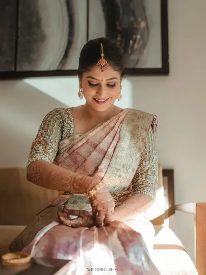 The bride in a quiet moment, admiring her bangles. The soft, natural light from the window creates a beautiful, painterly effect.