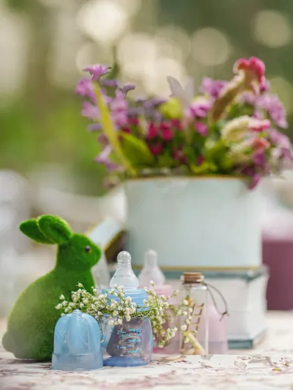 A close-up of a centerpiece with a green rabbit, baby bottles, and a teacup, all adorned with delicate flowers.