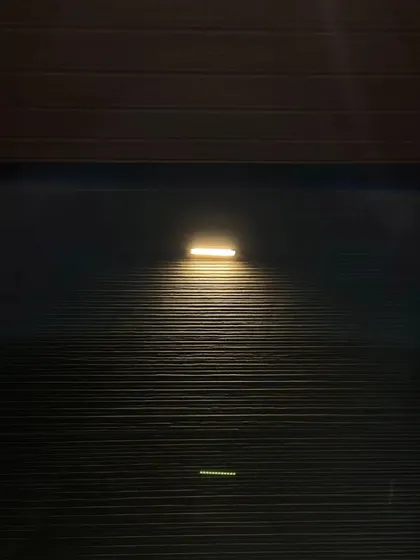 A single wall washer light illuminates a textured black wall, creating a dramatic and moody accent.