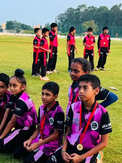 Young players with their medals and trophy, posing for a photo with their coach watching over them.