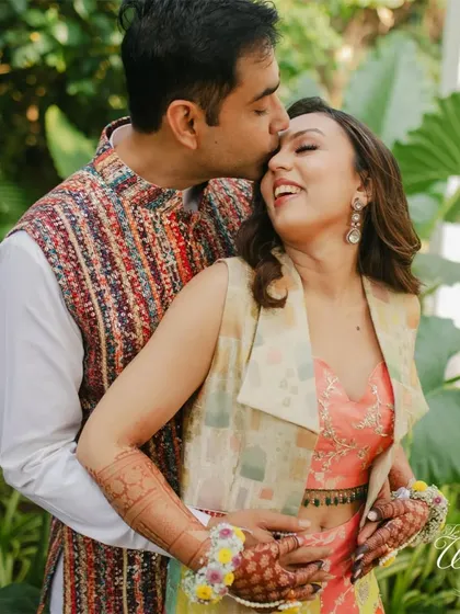A joyful hug from behind, the groom surprising the bride with a tender kiss on the head during their Haldi photoshoot.