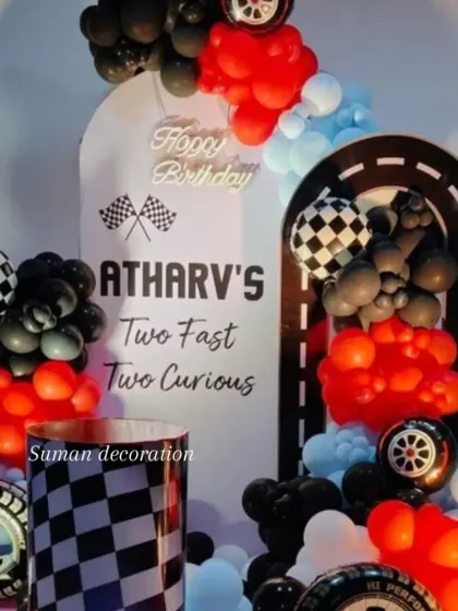A "Two Fast Two Curious" race car theme for a second birthday. The decor includes a custom arched backdrop, checkered flag details, and balloon arrangements in red, black, and blue.