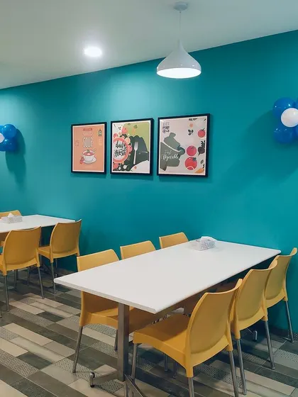 A section of the TVS canteen with a bold teal accent wall. The simple, modular furniture allows for flexible seating arrangements, accommodating both large groups and individual diners.
