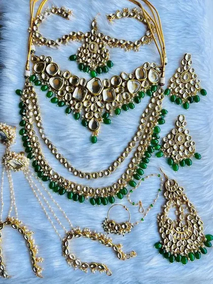 This is a complete Jadau Kundan bridal set with beautiful green beads and uncut stones. The rental package includes layered necklaces, a statement nath (nose ring), hath phool (hand harness), and oversized earrings for a truly royal look.