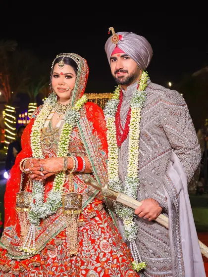 A traditional portrait of the couple on their wedding day. The bride's red lehenga and the groom's grey sherwani with a red necklace create a beautifully coordinated look.