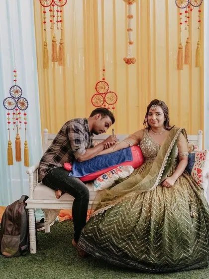 A quiet moment during the bridal mehendi application. The decor, with its bright yellow drapes and hanging dreamcatchers, creates a cheerful and relaxed setting.