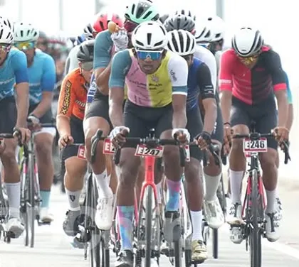 The peloton moves as one organism, with riders from different teams sharing the workload at the front. This is a classic scene from the Bangalore Classic Road Race.